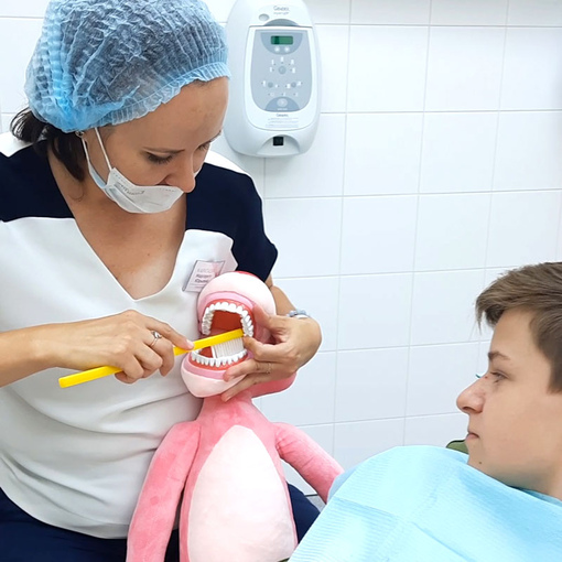 Врач-стоматолог объясняет ребенку как правильно чистить зубы